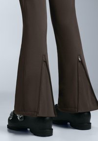 Barna szárában kicsit bővülő nadrágok oldalzippzárral a szegélyen és sima, rugalmas anyagból. Vastag fekete lábbelivel párosítva.