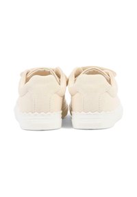 Zapatillas deportivas de lona beige con un corte superior de tela texturizada, bordes ondulados y suelas de goma blancas. Sin marca visible en la parte trasera.