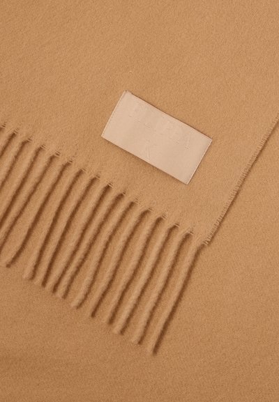 Καμήλινο κασκόλ από μαλλί με φουντωτές άκρες. Διαθέτει ορθογώνιο σχήμα και μια μπεζ δερμάτινη ετικέτα με τη σφραγίδα "FLIPPA K." Απαλή υφή.