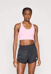 Jasnoróżowy sportowy biustonosz z szerokimi ramiączkami i zaokrąglonym dekoltem, w połączeniu z czarnymi sportowymi szortami z elastycznym pasem i detalem z logo.