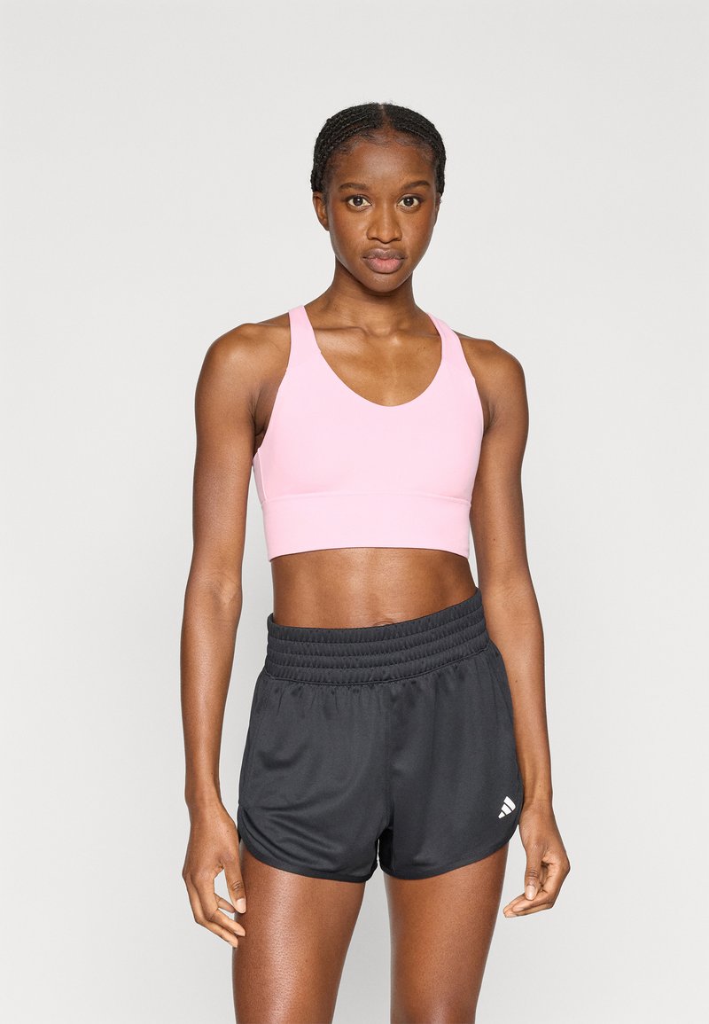 Jasnoróżowy sportowy biustonosz z szerokimi ramiączkami i zaokrąglonym dekoltem, w połączeniu z czarnymi sportowymi szortami z elastycznym pasem i detalem z logo.