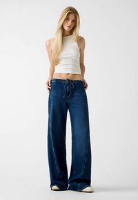 Vidde jeansbukser i mørkeblå med elastisk snøre i taljen, afslappet pasform og diskret falming. Glat tekstur, afslappet design.