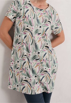 Vrouw draagt een losse beige top met korte mouwen met abstracte penseelstreekpatronen in groen, roze, zwart en bruin.