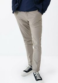 Béžové slim-fit kalhoty s hladkým povrchem a postranními kapsami, spárované s černobílými teniskami se šněrováním.