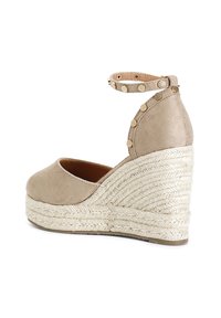 Béžové espadrilové sandály na klínu s kulatou špičkou, kotníkovými pásky a hřebíkovými akcenty. Texturovaný juteový podpatek měří přibližně 7,5 cm.