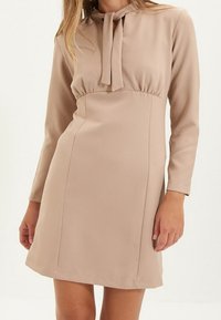 Abito beige a maniche corte con scollatura a lacci, corpino aderente e taglio dritto. Realizzato in tessuto liscio, presenta leggere arricciature in vita.