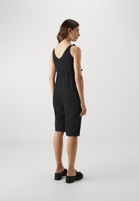 Zwarte jumpsuit met een v-hals en verstelbare banden, cincht op de taille, met een losse pasvorm en knielange pijpen.