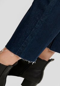 Mörkblå denimbyxor med fransade fållar, i kombination med svarta ankelstövlar med texturerad yta och klackar i blockstil.