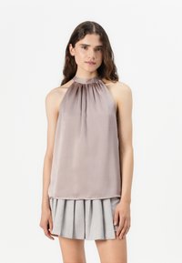 Helle lila Haltertop aus Satin, mit gerafften Ausschnittdetails. Kombiniert mit einem grauen Faltenrock.