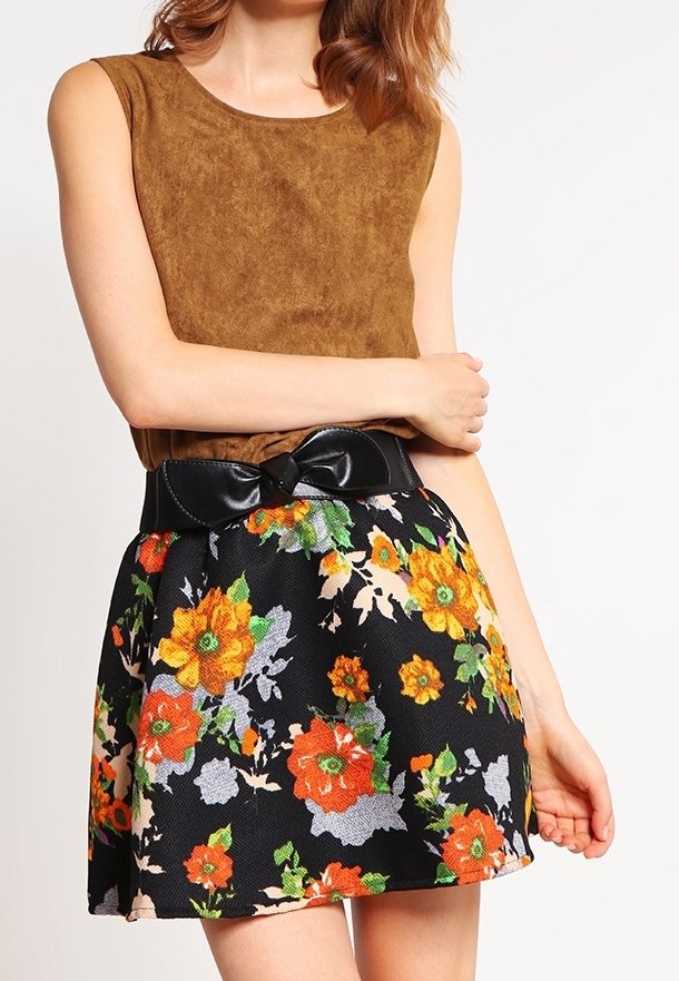 Braunes Wildleder-Top ohne Ärmel, kombiniert mit einem schwarzen Rock mit Blumenmuster, der orangefarbene und gelbe Blumen zeigt, und akzentuiert durch einen schwarzen Schleifen-Gürtel.