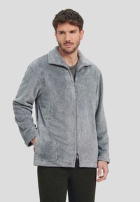 Chaqueta de pana gris con cierre de cremallera en el frente, cuello con solapa y bolsillos laterales. Presenta una textura suave y un diseño de corte relajado.
