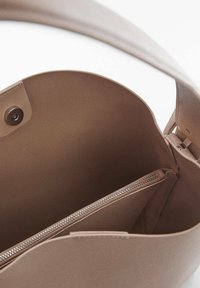 Beige læderhåndtaske med en blød tekstur, en lynlåslukket indvendig lomme og en magnetisk lukning. Rundet form og justerbar rem.