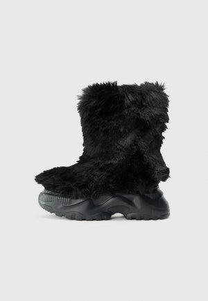 Black furry ankle boot with a textured upper, featuring a thick black rubber sole and treaded pattern for grip and stability.