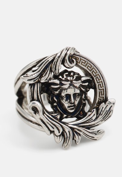 Anillo de plata con un diseño circular que presenta una cara central y acentos de hojas fluidas. Los detalles incluyen un patrón de clave griega alrededor del borde.