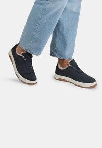 Jūras spēku sporta apavi ar zamša materiālu, baltu zoli un kažokādas oderi ap potīti. Iespējas ar auklu aizdari un teksturētu virsmu.