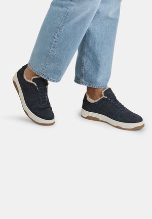 Tumedad sneakers, millel nahk ja valge tallaga, karvane vooder pahkluude ümber. Omab lipsuga disaini ja tekstuurset pinda.