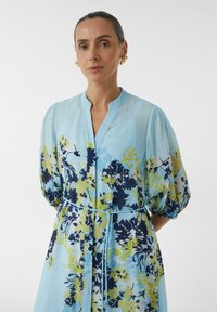 Blumenmaxikleid in Hellblau, mit lebhaften Marineblau-, Grün- und Gelbtönen, Mandarin-Kragen und gerüschten kurzen Ärmeln.