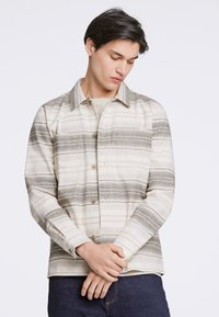 Camicia a righe beige e grigia con bottoni frontali, colletto a punta e maniche lunghe. Tessuto morbido con una sottile trama.
