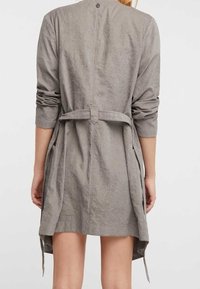 Vestido de tela ligero y gris con mangas largas, cinturilla y bolsillos laterales. Presenta una abertura en la parte posterior y detalles de costura simples.