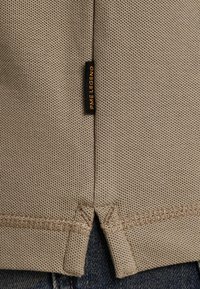 Beige textielshirt met een etiket waarop "PME Legend" staat. Heeft een gespleten zoom en contraststiksels aan de onderzijde.