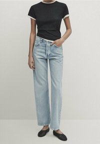 T-shirt nera a maniche corte con bordi bianchi abbinata a jeans a gamba larga azzurri, con vita alta e classica trama in denim.