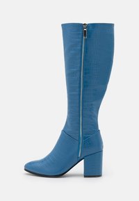 Bottes bleues montantes jusqu'aux genoux en matière à motif crocodile, avec une fermeture éclair latérale et un talon bloc. Bout pointu.