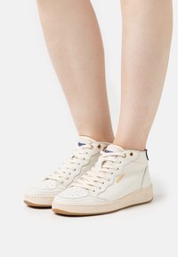 Cremfarbene Leder-High-Top-Sneaker mit durchbrochenem Zehenbereich, goldenen Ösen und beige-gummierter Sohle, ausgestattet mit einem marineblauen und goldenen Logo-Tag auf der Zunge.