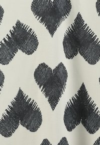 Cuori neri dipinti a pennello su uno sfondo di tessuto beige chiaro, con un aspetto testurizzato e pattern regolarmente distanziati.
