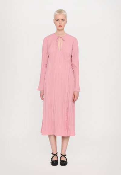 Robe midi rose en tissu texturé, avec des manches longues et un détail d'encolure en forme de clé. La robe présente des liens sur les côtés et une silhouette fluide.
