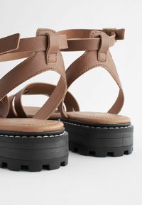 Braune Leder-Plateausandalen mit Mehrfachriemen-Design, verstellbarem Schnallenverschluss, strukturiertem Fußbett und schwarzer Gummisohle mit Profilmuster.