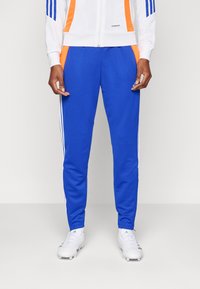 Blue athletic pants with white side stripes, made from a smooth, flexible fabric. Features contrasting orange accents and a fitted design.