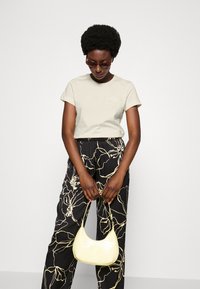 Camiseta beige de manga corta con logotipo, combinada con pantalones negros que tienen líneas florales blancas, y un pequeño bolso amarillo con textura de cocodrilo.