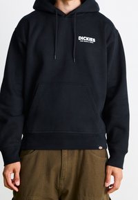 Sweat à capuche noir en mélange de coton, avec une poche avant, des cordons de serrage, et un logo blanc. Les poignets et l'ourlet côtelés ajoutent de la texture.