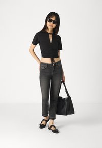 Svart avskåret topp med sammenkrøpne detaljer, lyse denim jeans, svart totebag, og flate svarte sko med spenneaksenter.
