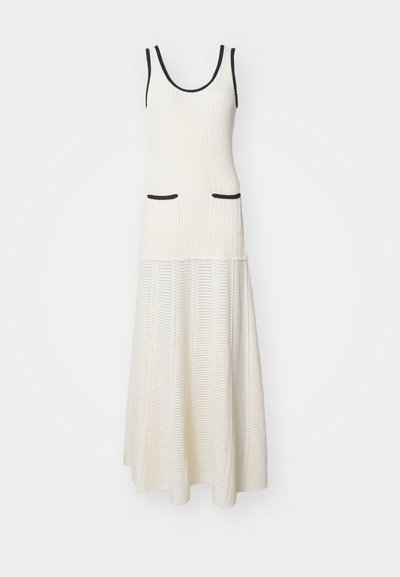 Vestido maxi blanco de canalé que presenta un top ajustado con escote redondeado, dos bolsillos frontales y un ribete negro en los orificios de los brazos.