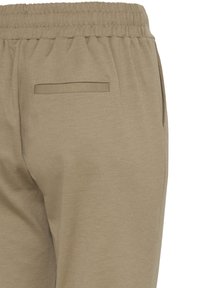 Beige joggers with an elastic waistband, side pockets, and a small back pocket. Made of soft jersey material with a smooth texture.