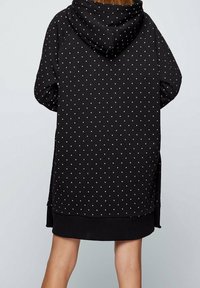 Černé mikinové šaty s kapucí a bílým puntíkovým vzorem, s žebrovaným lemem a bočními rozparky pro lepší pohyblivost.