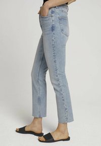 Ljusblå högmidjade jeans med rak ben och fransad fåll, tillverkade av denimtyg. Matchas med svarta slide-sandaler.