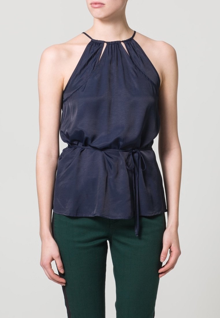 Marinblå halternecktop med samlad nacke, åtsittande midja och knytdetalj; tillverkad av ett lätt, slätt tyg. Matchad med gröna byxor.