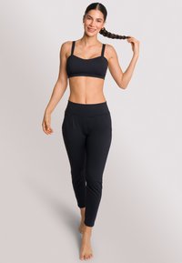 Zwarte sport-bh met dunne bandjes en naadloos ontwerp, gecombineerd met zwarte, taps toelopende legging met een hoge taille en zijzakken.