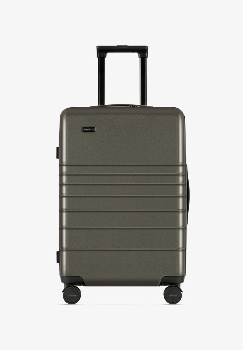 Twarda walizka w oliwkowym kolorze, z rowkowanym wzorem, czarnym uchwytem i czterema kółkami zapewniającymi łatwość w poruszaniu się.