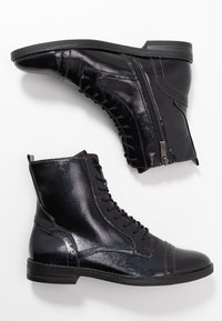 Bottines en cuir noir avec une finition brillante, à lacets à l'avant, fermeture éclair sur le côté, semelle plate et détails surpiqués le long de la tige.