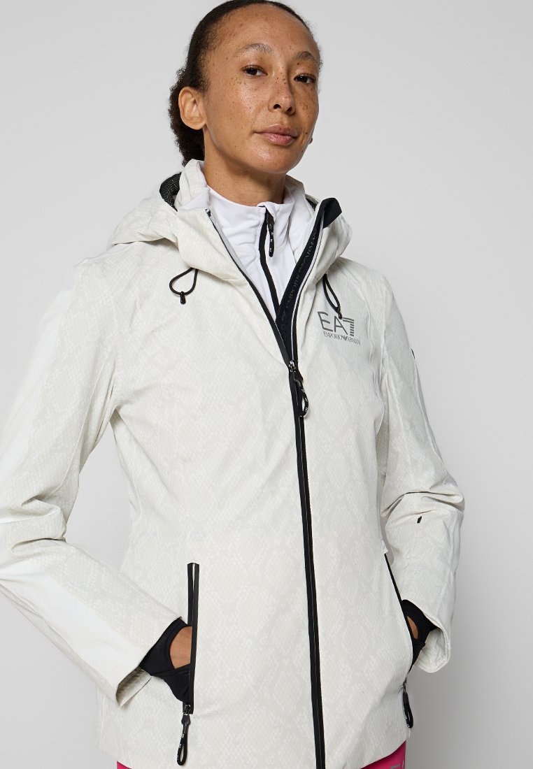 Weiße wasserdichte Jacke mit strukturiertem Rautenmuster, schwarzem Reißverschluss, verstellbarem Kapuze und schwarzen Akzenten an den Säumen und Taschen.