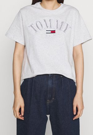 Person iført en lysegrå Tommy Jeans t-shirt og højttaljede mørkeblå jeans, vist fra nakke til hofter.