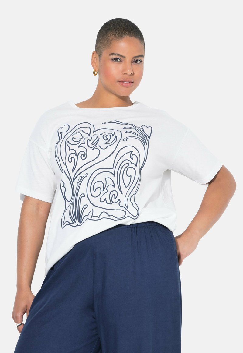 Witte katoenen T-shirt met een marineblauw abstract hartontwerp, korte mouwen en een relaxte pasvorm, gecombineerd met marineblauwe wijde broek.