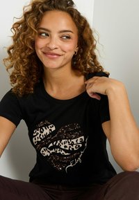 Camiseta negra de manga corta con un diseño de corazón de estampado de leopardo con lentejuelas en tonos de negro y beige. Escote redondo, tejido suave.