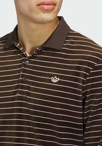 Brown striped polo shirt with pink horizontal stripes, three-button placket, and small white embroidered logo on the chest.