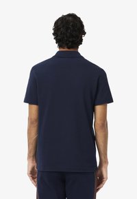 Niebieska koszulka polo wykonana z bawełny, z klasycznym kołnierzykiem, krótkimi rękawami i prostym dołem, pokazana z tyłu.