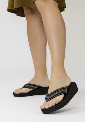 Chanclas negras con una correa texturizada que cuenta con acentos metálicos y una suela de plataforma gruesa. El diseño es minimalista y funcional.