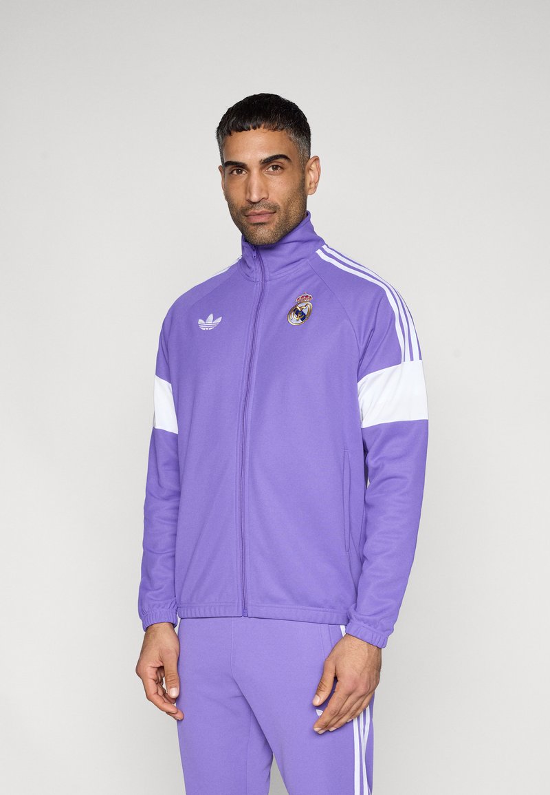 Μωβ αθλητικό μπουφάν με λευκές λεπτομέρειες, κλείσιμο με φερμουάρ και ψηλό γιακά. Διαθέτει λογότυπο και τρεις λευκές ρίγες στα μανίκια. Κατασκευασμένο από υλικό που αναπνέει.